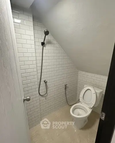 Compact bathroom with sloped ceiling and modern white subway tiles.