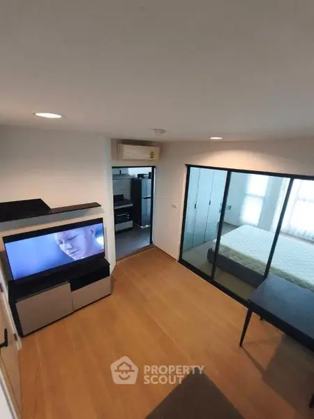 Modern apartment with open living room and bedroom, featuring sleek wooden flooring and built-in storage.