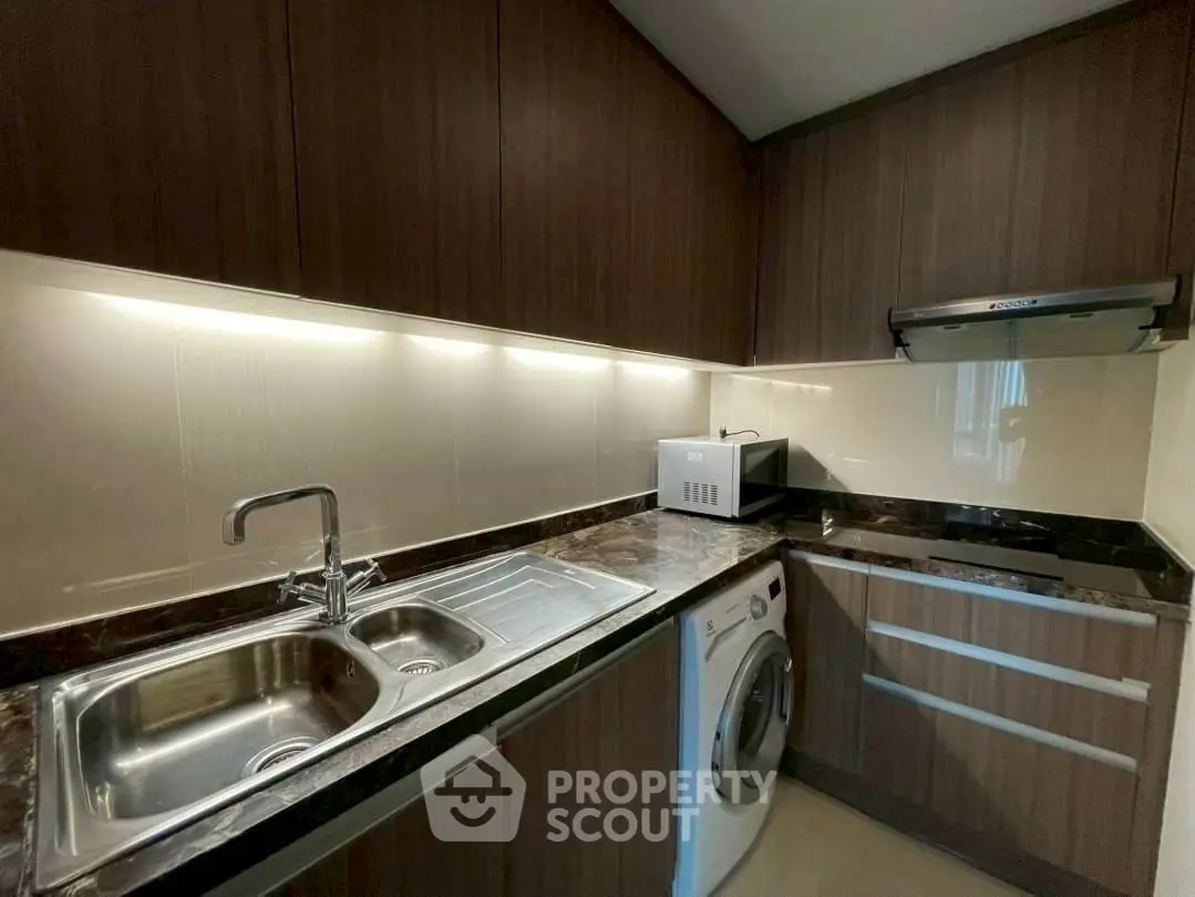 Modern kitchen with sleek cabinetry, washing machine, and microwave in compact layout.