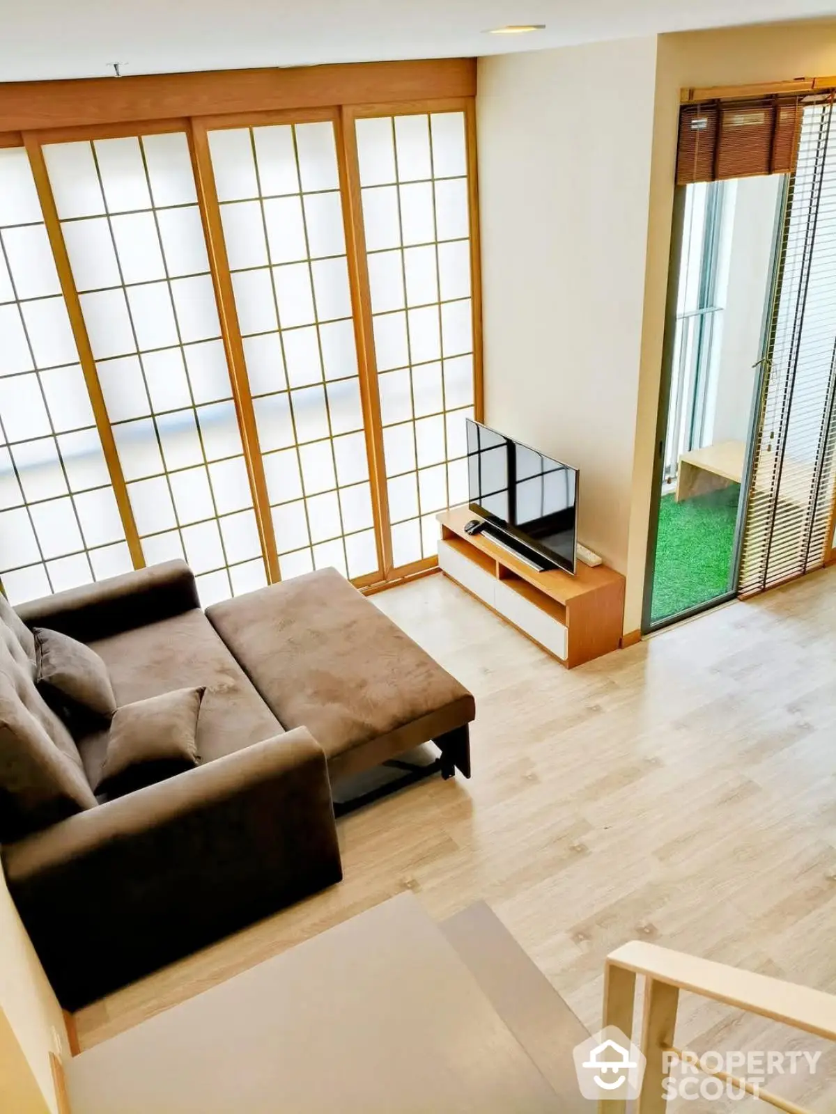 Modern living room with cozy sofa and TV, featuring large windows and natural light.