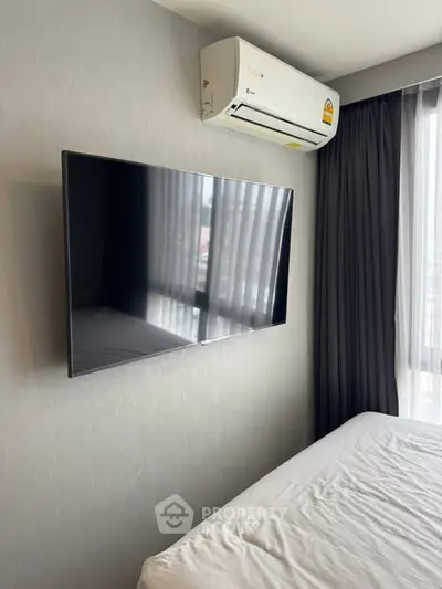 Modern bedroom with wall-mounted TV and air conditioning unit, featuring sleek design and natural light.
