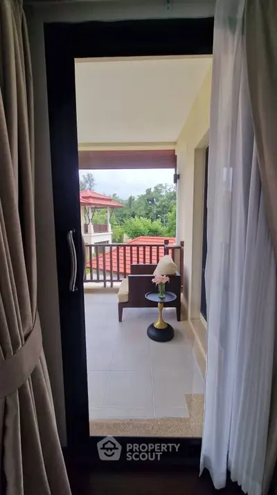 Charming balcony view from a cozy interior, featuring lush greenery and elegant outdoor seating.