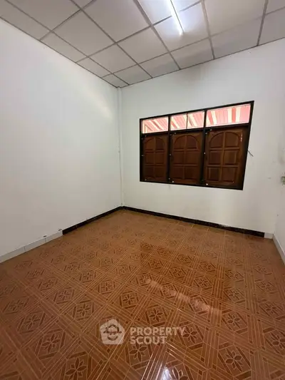 Spacious empty room with tiled floor and wooden windows, perfect for customization.
