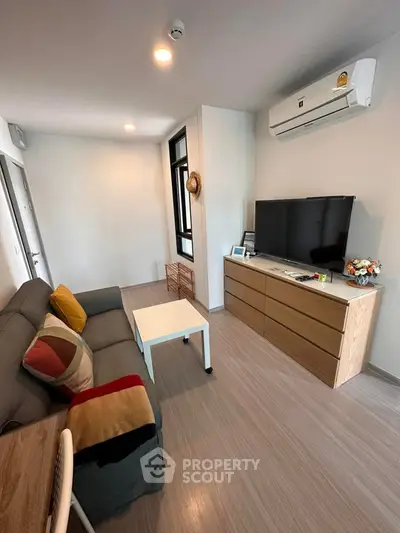 Modern living room with sleek design, featuring a cozy sofa, flat-screen TV, and air conditioning unit.