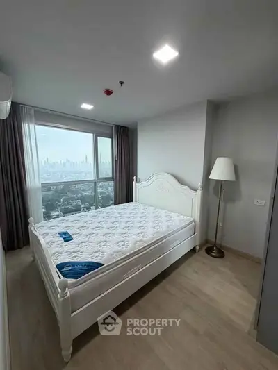Spacious bedroom with city view, featuring elegant white bed and floor lamp, perfect for urban living.