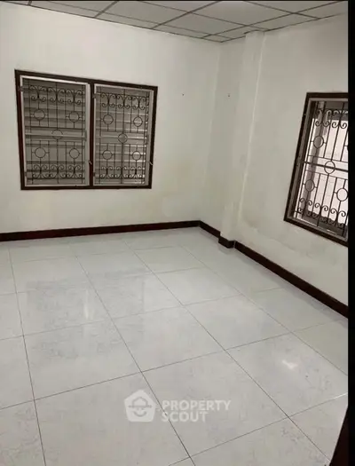 Spacious empty room with tiled floor and barred windows, ideal for customization.