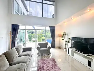 Spacious living room with high ceiling and pool view, featuring modern furniture and natural light.