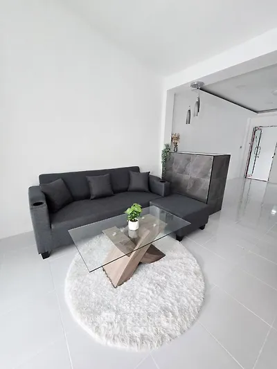 Modern living room with sleek gray sofa and stylish glass coffee table on plush white rug.