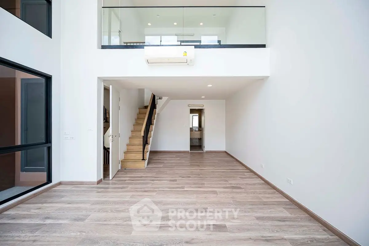 Spacious modern living room with high ceiling and mezzanine, featuring elegant wooden flooring.