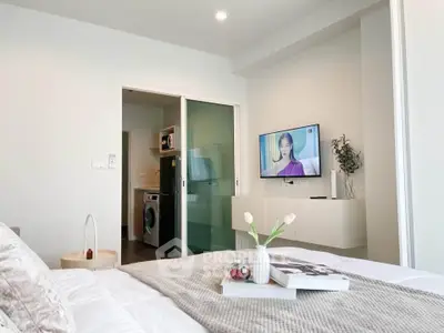 Modern bedroom with TV and compact kitchen featuring washing machine and microwave.