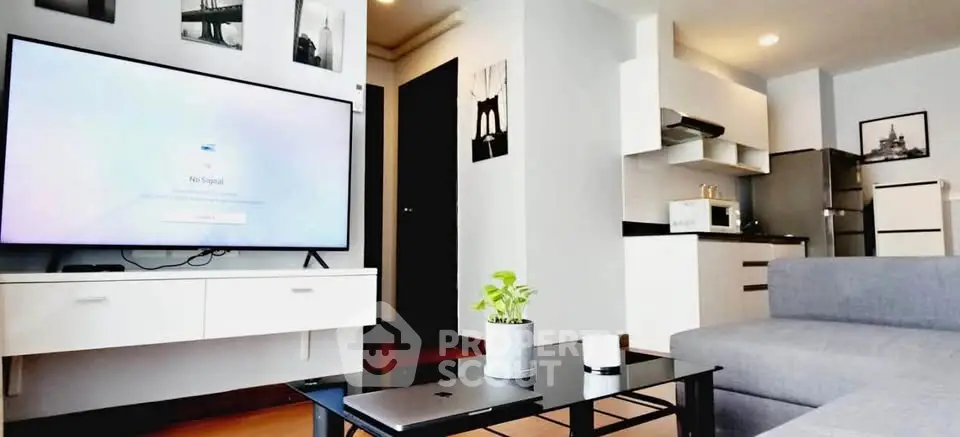 Modern living room with sleek furniture and open kitchen layout, featuring a large TV and stylish decor.