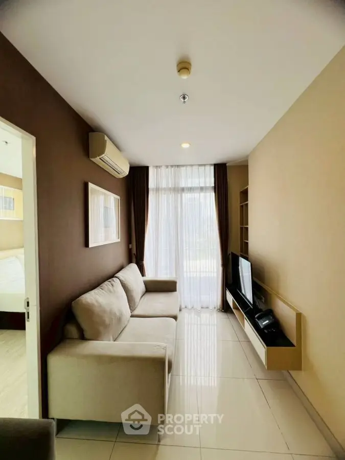Modern living room with cozy beige sofa and sleek TV unit, featuring large window for natural light.
