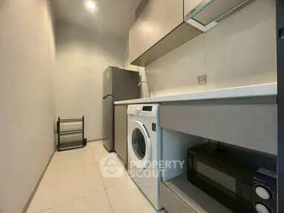Modern compact kitchen with washing machine and microwave in sleek apartment.