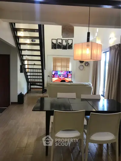 Modern living room with open staircase and dining area, featuring stylish lighting and contemporary decor.