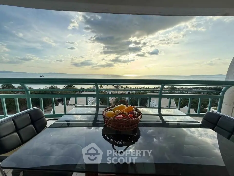 Stunning balcony view with glass table overlooking ocean sunset, perfect for relaxation.
