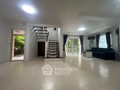 Spacious living room with modern staircase and large windows offering natural light.