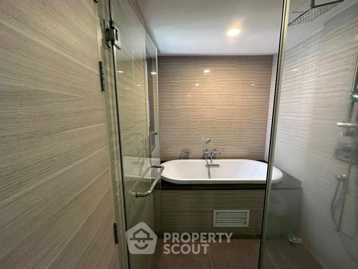 Modern bathroom with glass shower and built-in bathtub in stylish apartment.