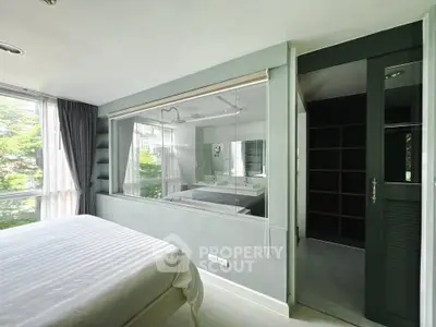 Modern bedroom with large window and ensuite bathroom featuring glass partition.