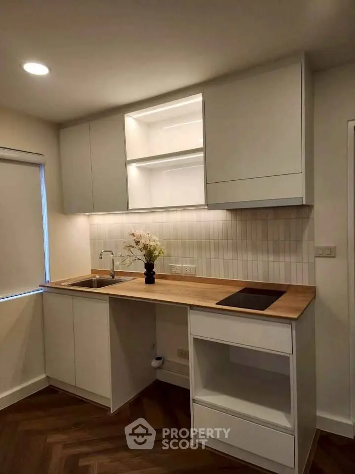 Modern minimalist kitchen with sleek white cabinets and wooden countertop, featuring an induction cooktop and stylish backsplash.
