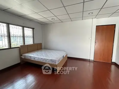 Spacious bedroom with wooden flooring and large window for natural light.