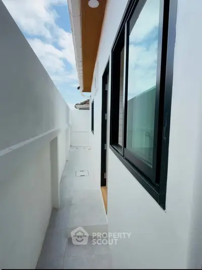 Modern narrow balcony with sleek windows and white walls, offering a minimalist outdoor space.