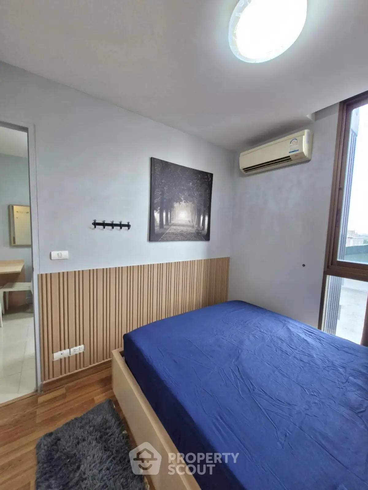 Cozy bedroom with blue bedding and wall art, featuring air conditioning and wooden flooring.