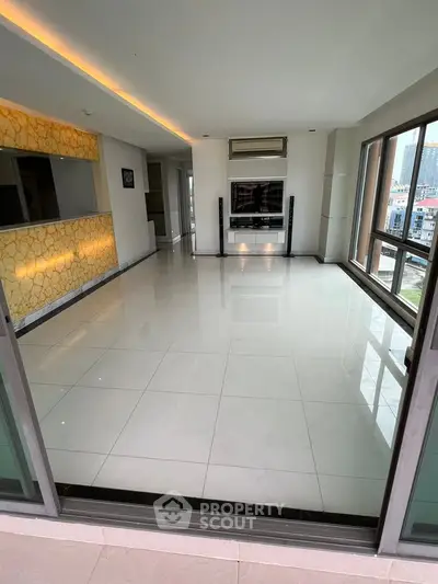 Spacious modern living room with large windows and city view, featuring sleek tile flooring and ambient lighting.