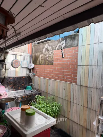 Charming outdoor kitchen area with rustic brick and wood paneling, featuring a stainless steel sink and lush greenery.