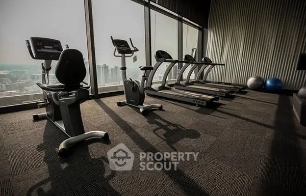 Modern gym with city view and exercise equipment in high-rise building.