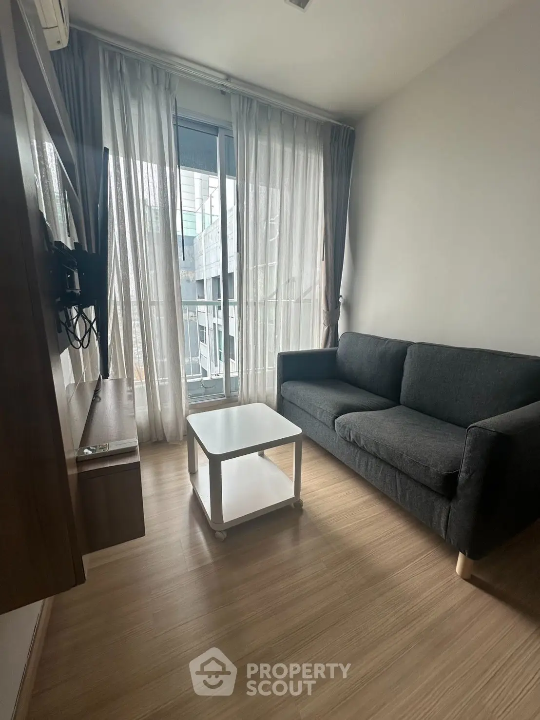 Cozy living room with modern sofa and TV, featuring floor-to-ceiling windows and wooden flooring.