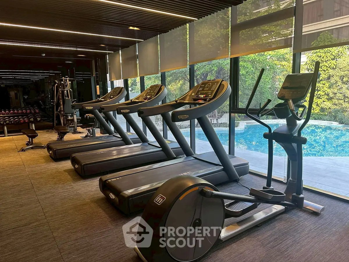 Modern gym with treadmills and pool view in luxury apartment complex.