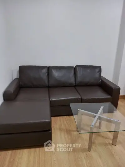 Modern living room with sleek brown leather sofa and glass coffee table on wooden floor.