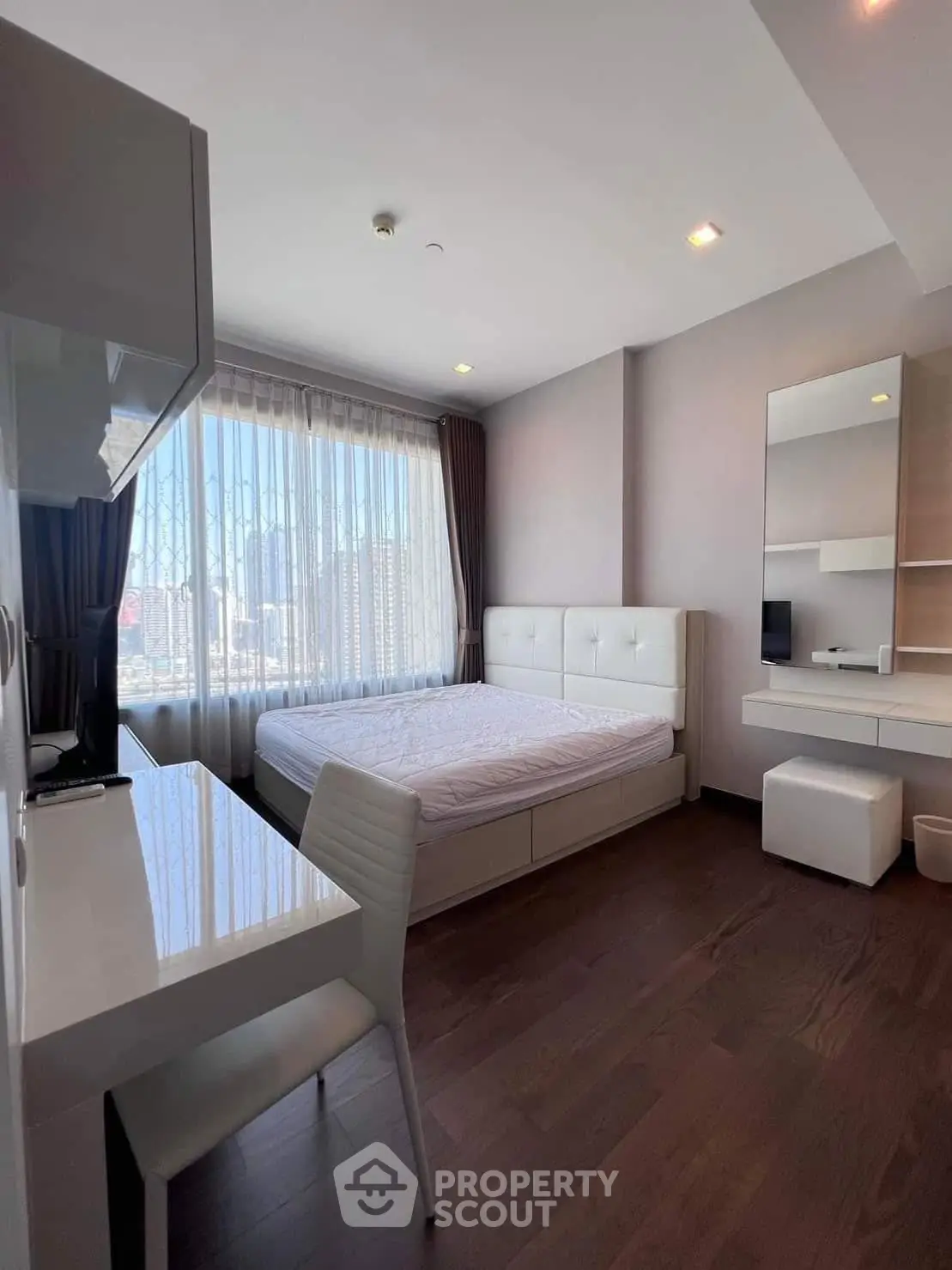 Modern bedroom with large window and sleek furnishings in a high-rise apartment.