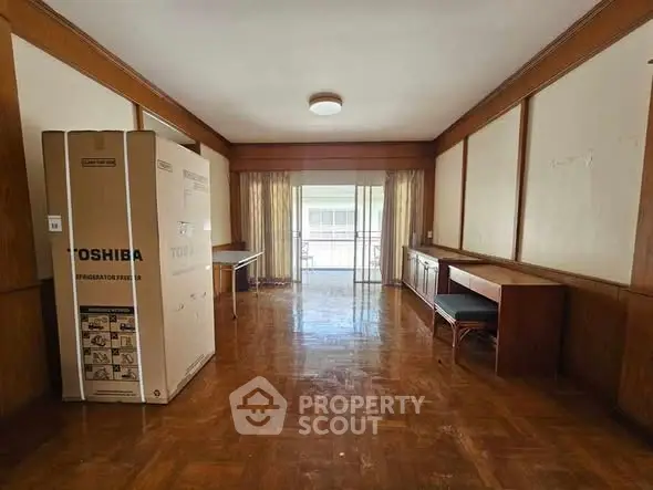 Spacious living room with wooden flooring and balcony access, featuring a new refrigerator.
