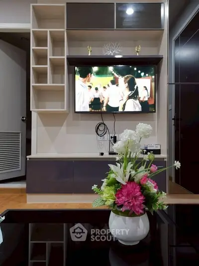Modern living room with wall-mounted TV and stylish shelving, featuring a vibrant floral centerpiece on a sleek table.