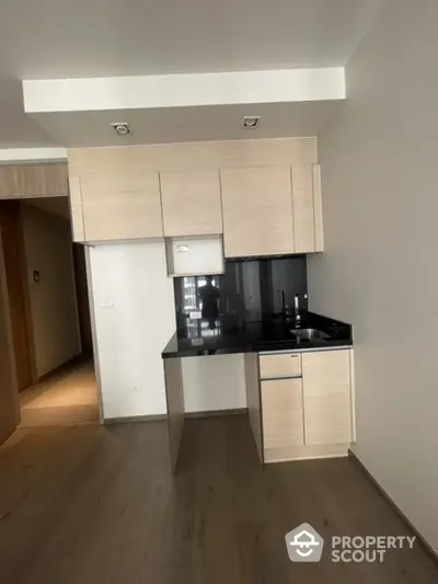 Modern minimalist kitchen with sleek cabinetry and black countertop in open layout apartment.