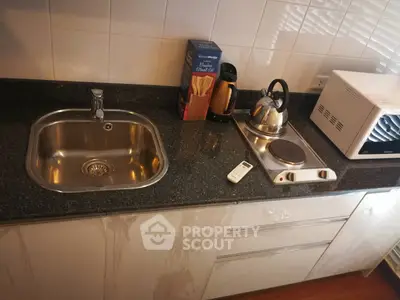 Modern kitchen with sleek countertop, sink, and appliances including a kettle and microwave.