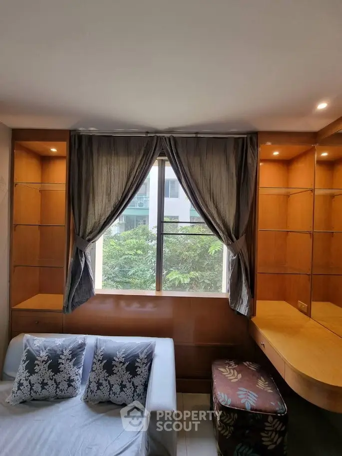 Cozy living room with large window and built-in wooden shelves, offering a serene view of greenery.