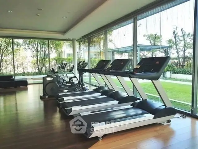 Spacious gym with modern treadmills and garden view in luxury apartment complex.
