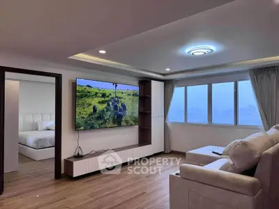 Spacious modern living room with large TV and cozy seating area, adjacent to a stylish bedroom.