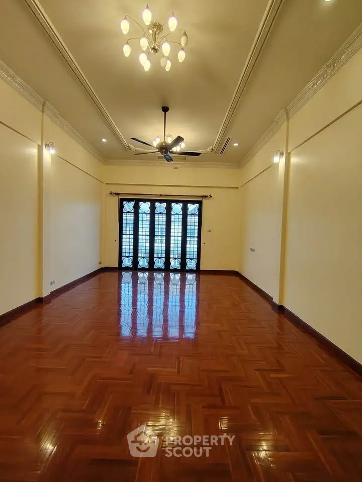 Spacious living room with elegant chandelier and polished wooden flooring.