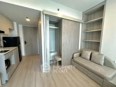 Modern apartment interior with open kitchen and cozy living area featuring built-in shelves and light wood flooring.