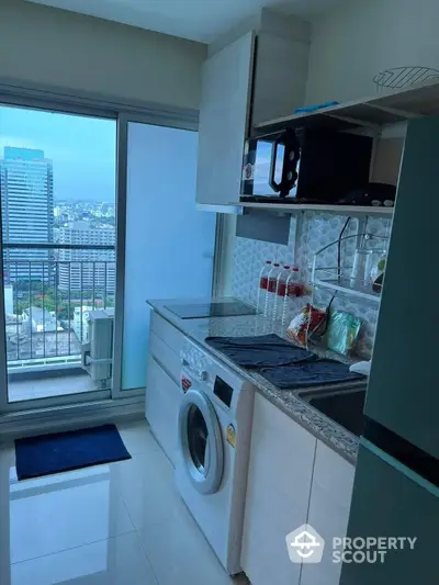 Compact urban kitchen with modern appliances, granite countertop, and a stunning city view through the balcony doors, perfect for cosmopolitan living.