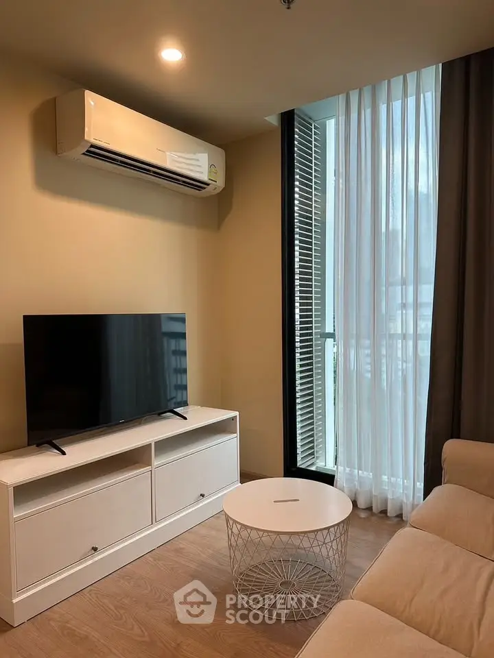 Modern living room with TV, air conditioning, and natural light from large window.