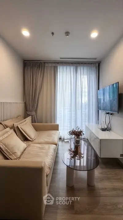 Cozy living room with elegant sofa, modern TV setup, and natural light through sheer curtains.