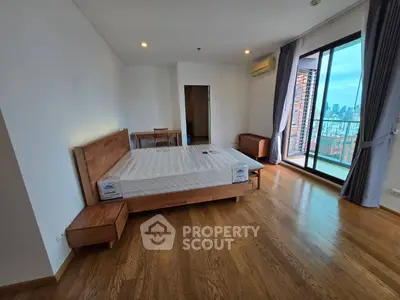Spacious bedroom with wooden flooring and city view balcony in modern apartment