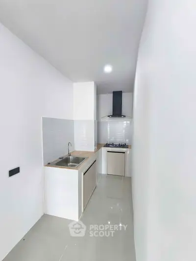 Modern minimalist kitchen with sleek white cabinetry and gas stove in compact layout.