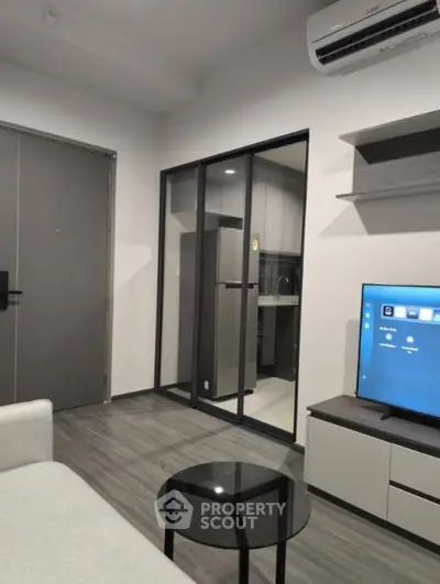 Modern living room with sleek furniture and open kitchen layout, featuring air conditioning and a flat-screen TV.