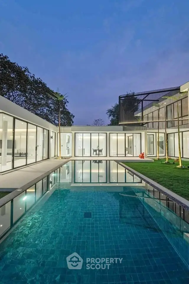 Luxurious modern home with stunning pool and expansive glass windows at dusk.