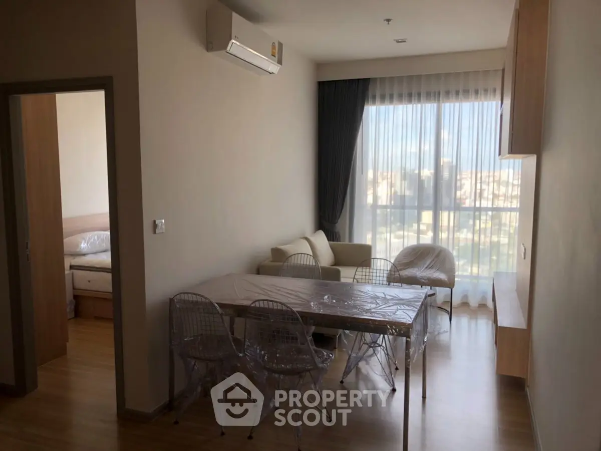 Modern living room with dining area and city view, featuring sleek furniture and natural light.